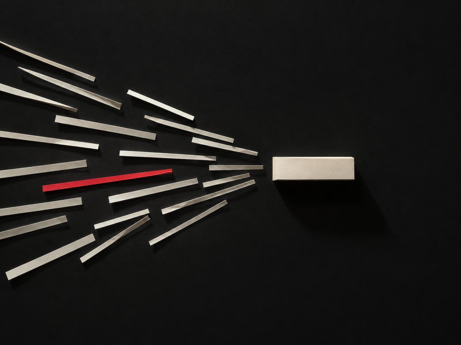 Scattered cream paper strips on a near-black surface converging into a single ordered stack, with one strip picked out in red