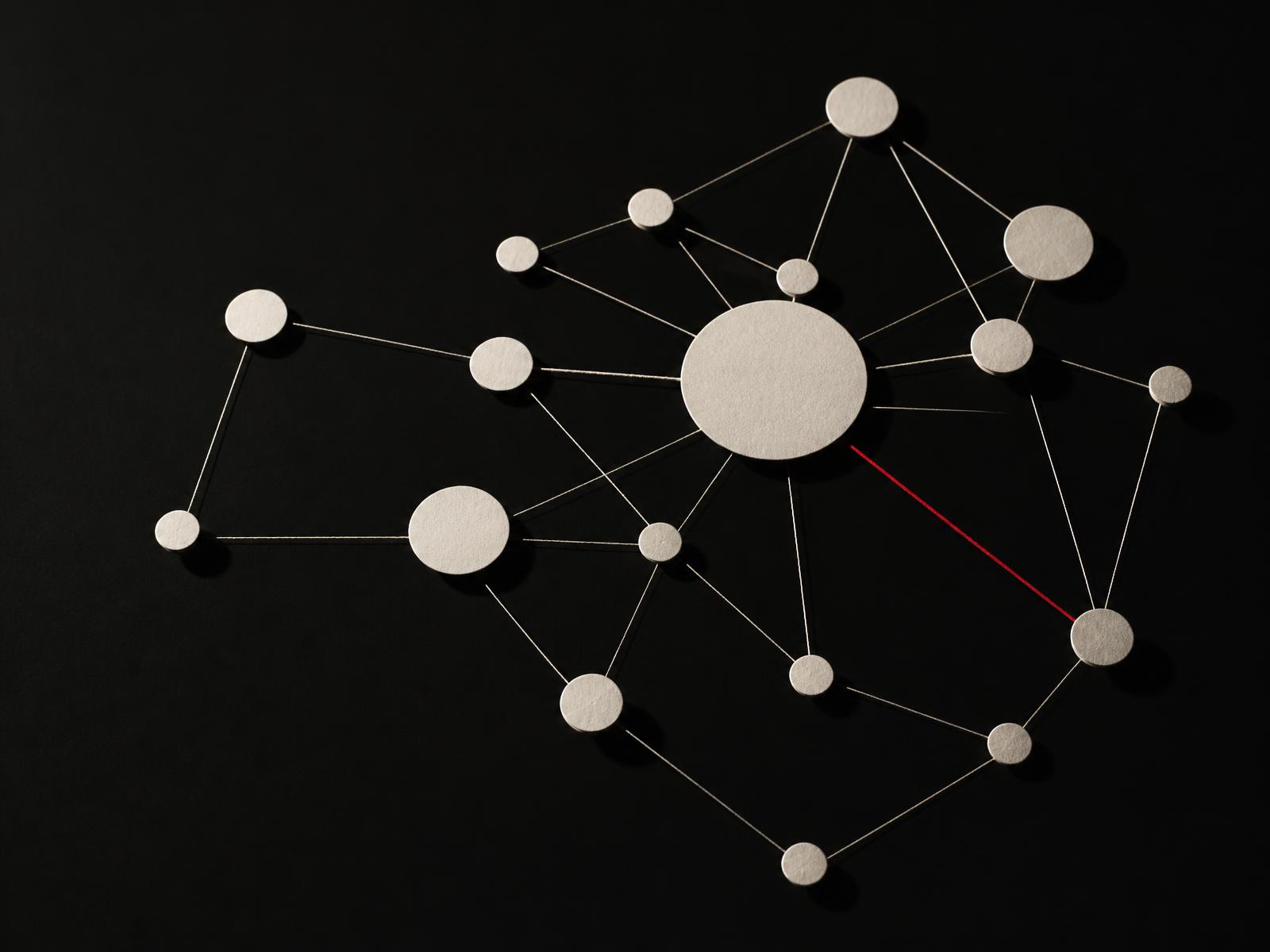 Cream paper discs of different sizes connected by fine threads into a network map on a near-black surface, with one thread picked out in red